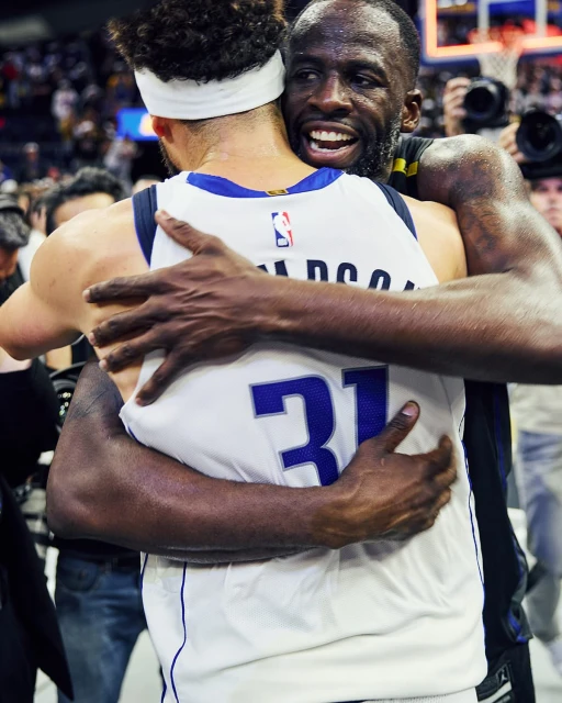 Two basketball players, one with number 31 on his jersey, embrace on the court in a display of sportsmanship, smiles, and camaraderie.