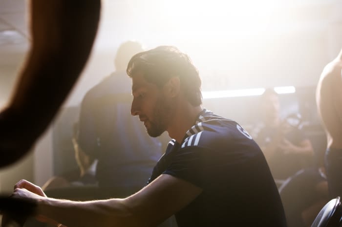 Athlete seated indoors wearing a dark athletic t-shirt with white stripes under strong backlighting.