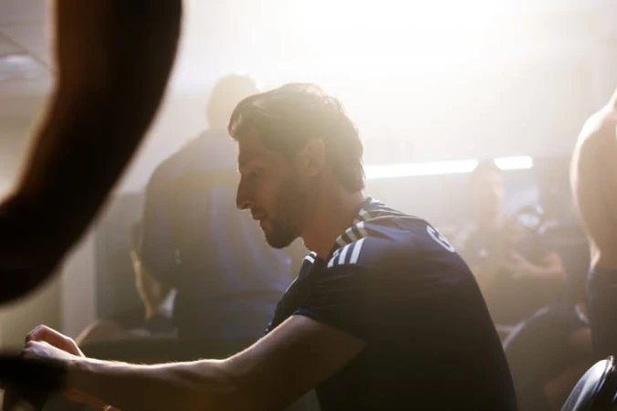 Athlete seated indoors wearing a dark athletic t-shirt with white stripes under strong backlighting.