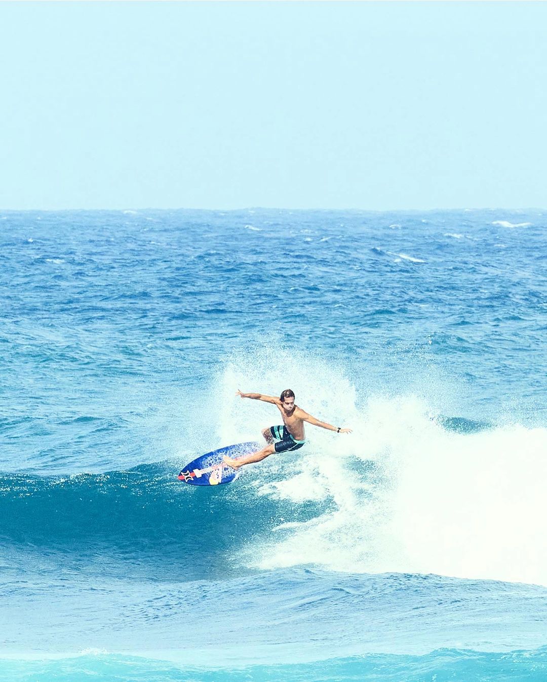 A surfer riding a wave on a bright, sunny day. The surfer is the main focus, with the blue ocean and sky creating a vibrant background.