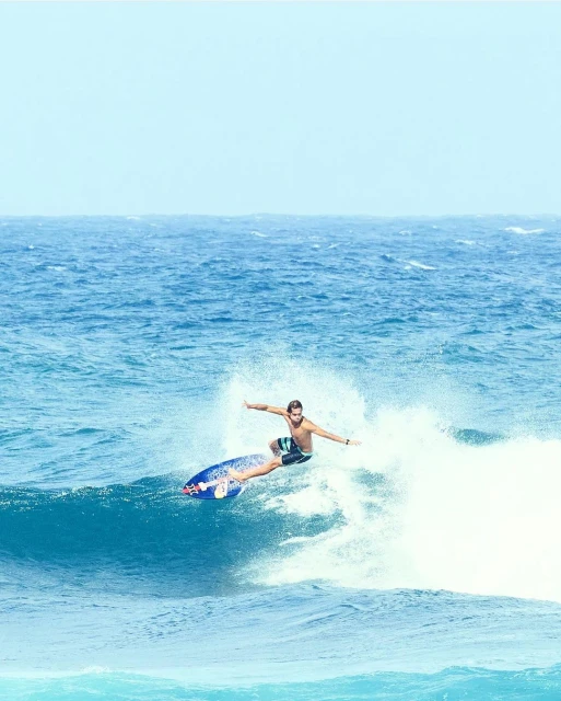 A surfer riding a wave on a bright, sunny day. The surfer is the main focus, with the blue ocean and sky creating a vibrant background.