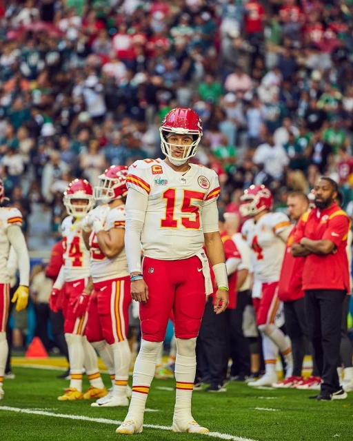 American football player Patrick Mahomes of the Kansas City Chiefs stands on the field during a game in a stadium filled with fans.