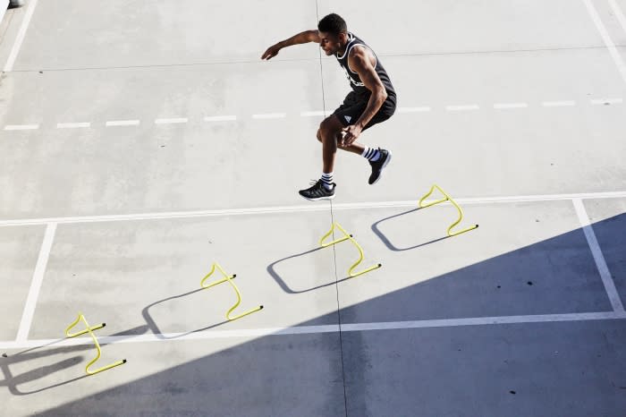 Athletic man in black sportswear leaps over yellow hurdles on a grey concrete surface, capturing a dynamic moment of fitness and agility.