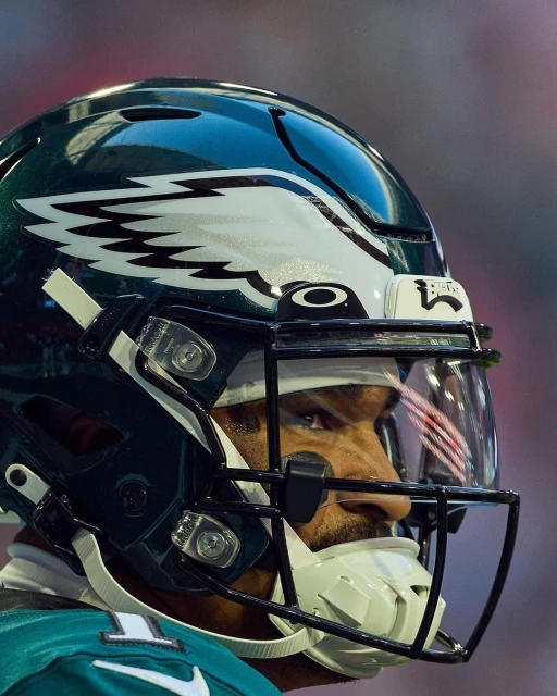 Close-up of an American football player in full helmet with visor, facing to the right, in a stadium setting.