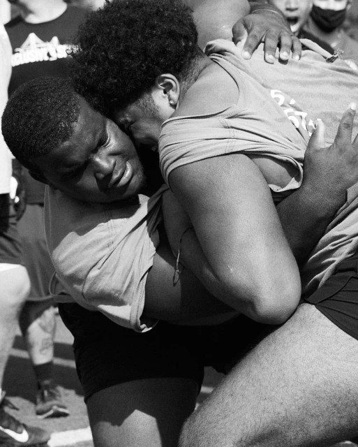 Two young men in a close embrace outdoors, captured in a black and white photograph showing their physical closeness and support.