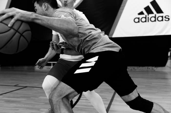 Two athletes in action with a basketball on a basketball court, sporting athletic wear with the Adidas logo in the background.