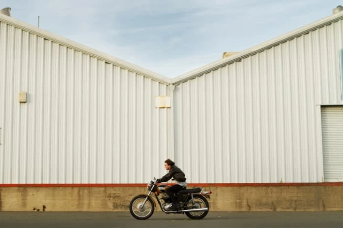Man riding a motorcycle past a large white industrial building exterior