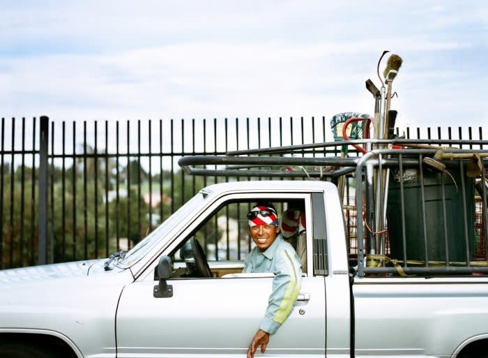 Man smiles from a silver pickup truck with cleaning tools in the truck bed. The photo shows a sunny, outdoor, daytime scene.