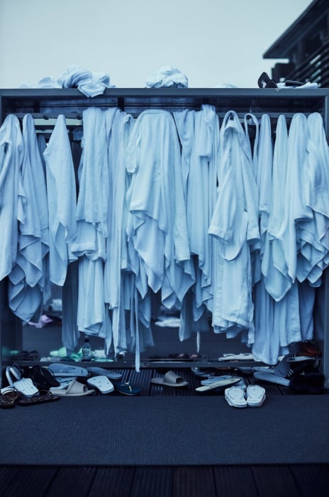 Rack filled with neatly hanging white bathrobes, complemented by an assortment of sandals and slippers lined beneath in neutral tones.