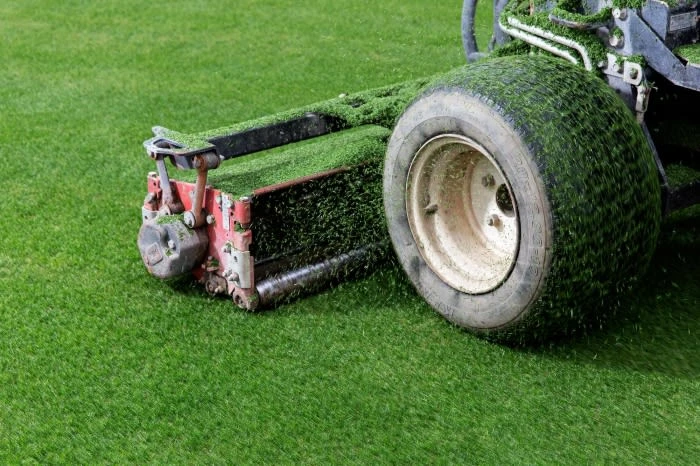 Artificial turf grooming machine with a roller and tires, used to maintain and groom synthetic grass on a sports field or lawn.