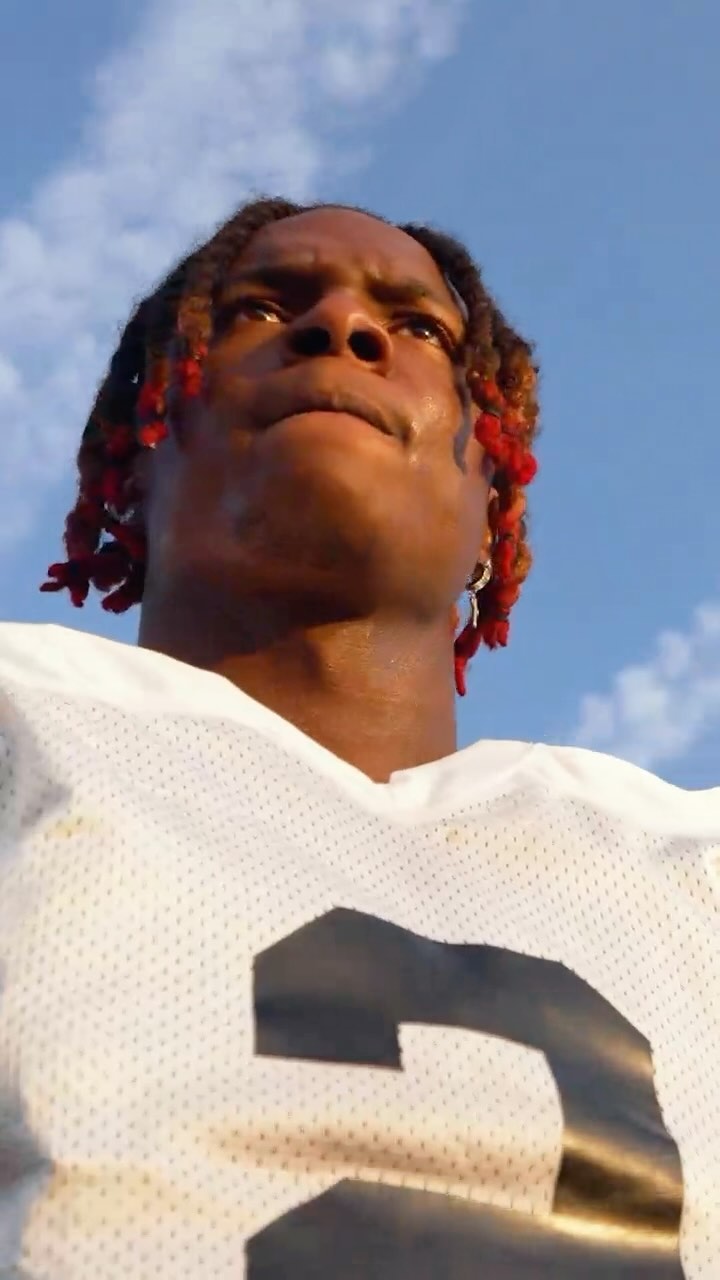 Close up of an adult male athlete in a football jersey looking up at the sky on a sunny day with clouds in the background.