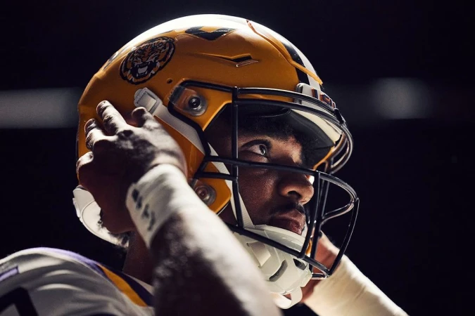 Close-up of a male football player wearing a yellow team helmet with logo, holding the sides of the helmet with gloved hands.