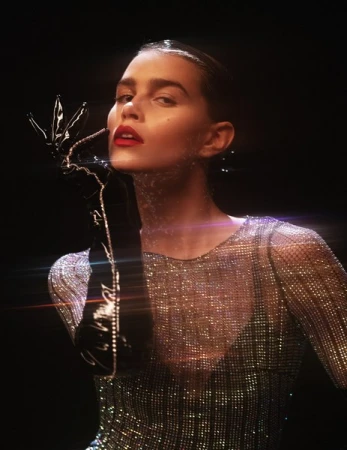 Elegant portrait of an adult woman with dark hair, red lipstick, and long black gloves, wearing a sparkling top, against a dark background.
