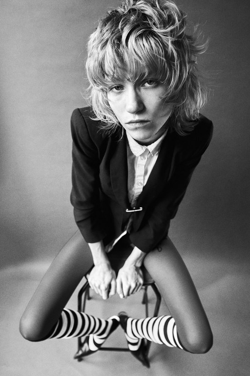 Monochrome portrait by Alessio Albi of a model with short textured hair seated on a stool wearing a blazer and striped socks.