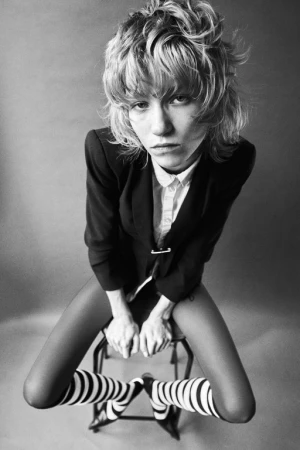 Monochrome portrait by Alessio Albi of a model with short textured hair seated on a stool wearing a blazer and striped socks.