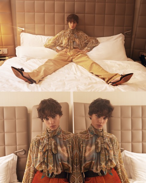 A woman in a patterned blouse and yellow pants lies on a white bed in a hotel room in a symmetrical, visually multiplied image.