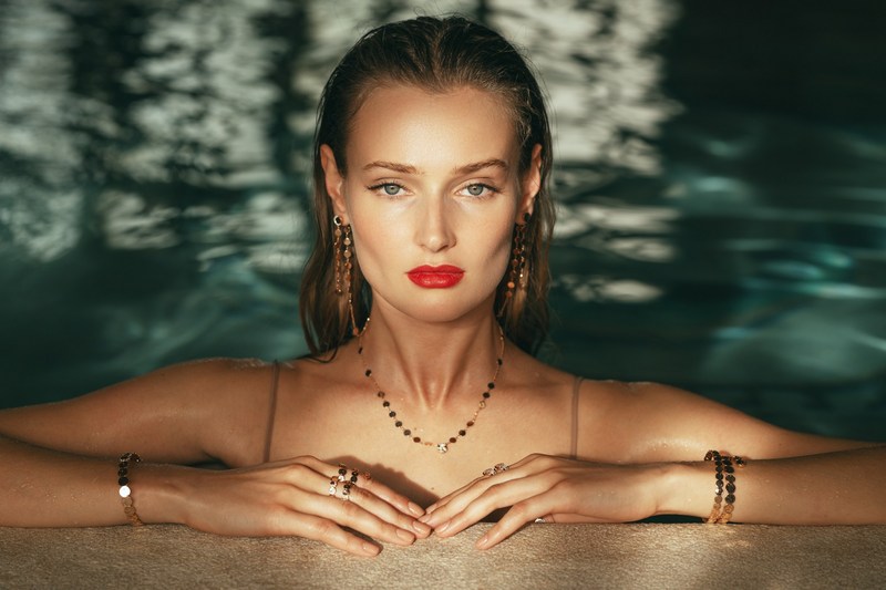 Portrait of a woman with wet hair and red lipstick wearing gold jewelry in a pool by Alessio Albi