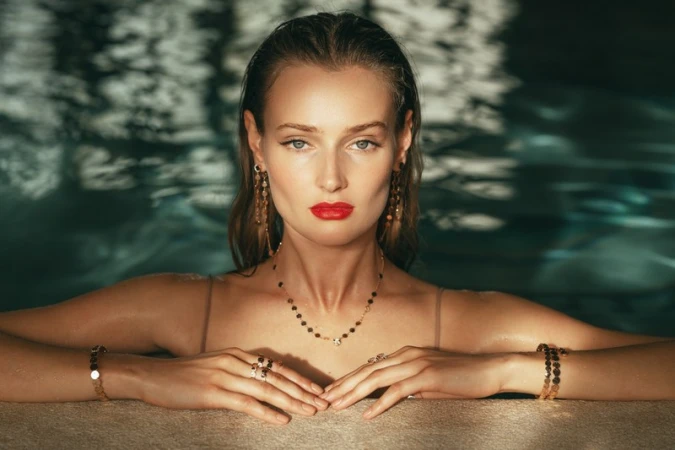 Portrait of a woman with wet hair and red lipstick wearing gold jewelry in a pool by Alessio Albi
