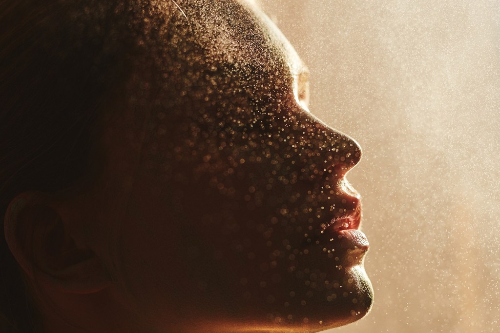 Profile of an adult woman's face covered in shimmering gold dust, captured in soft light, creating a magical and ethereal appearance.