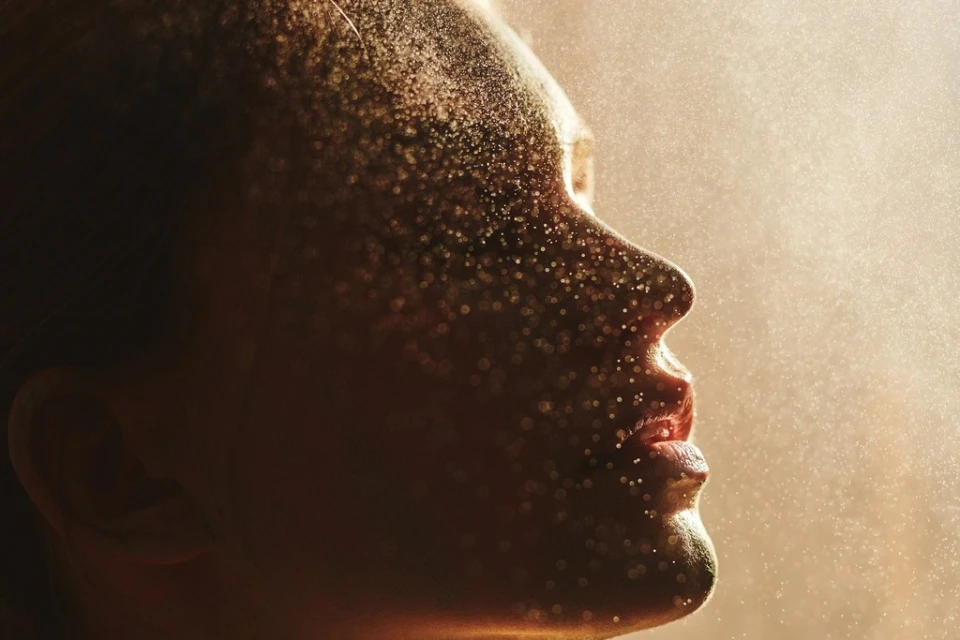 Profile of an adult woman's face covered in shimmering gold dust, captured in soft light, creating a magical and ethereal appearance.