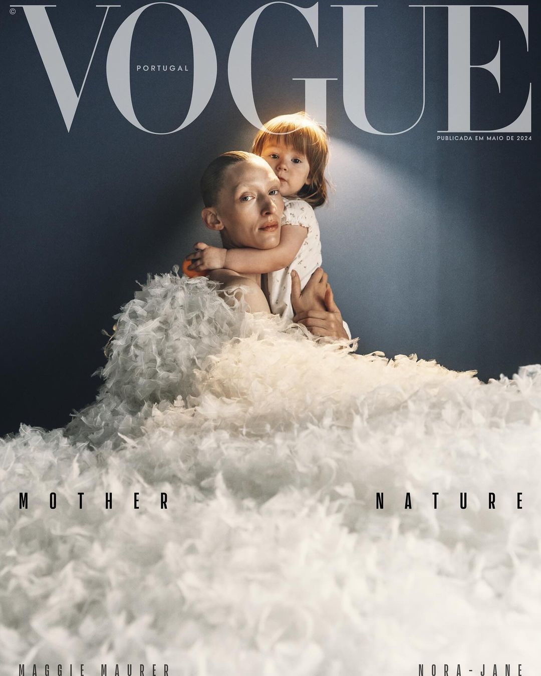 Vogue Portugal cover featuring an adult female model holding a young child, both adorned in a large white feathered garment, studio lit.