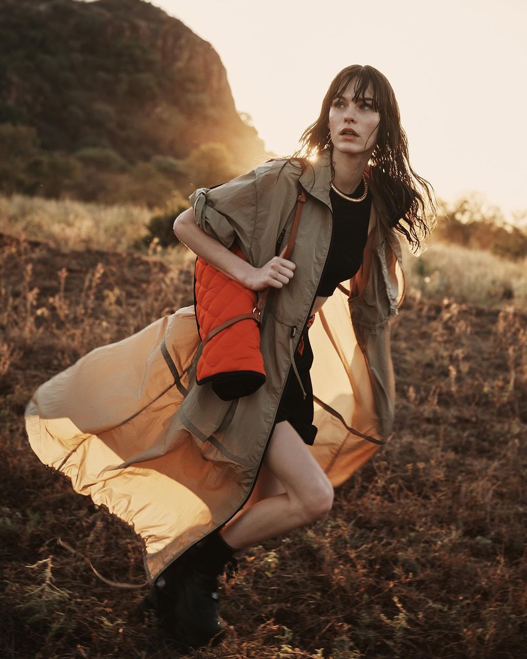 Woman in khaki coat running through a grassy field at sunset by Alessio Albi