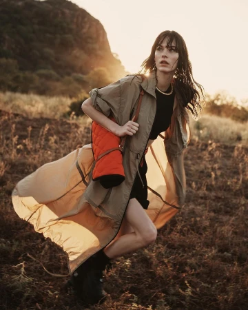 Woman in khaki coat running through a grassy field at sunset by Alessio Albi