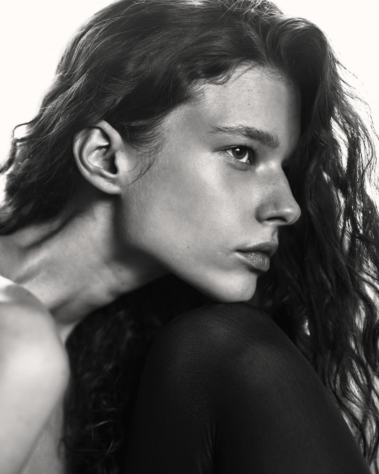 Black and white portrait of a young person with long wavy hair looking off-camera, focusing on their face and upper body.