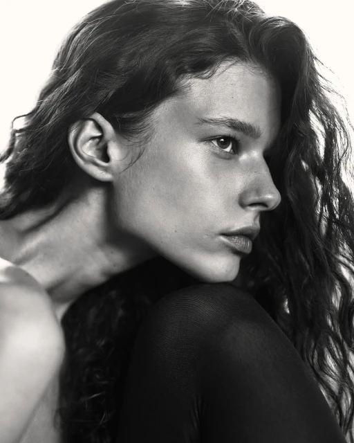 Black and white portrait of a young person with long wavy hair looking off-camera, focusing on their face and upper body.