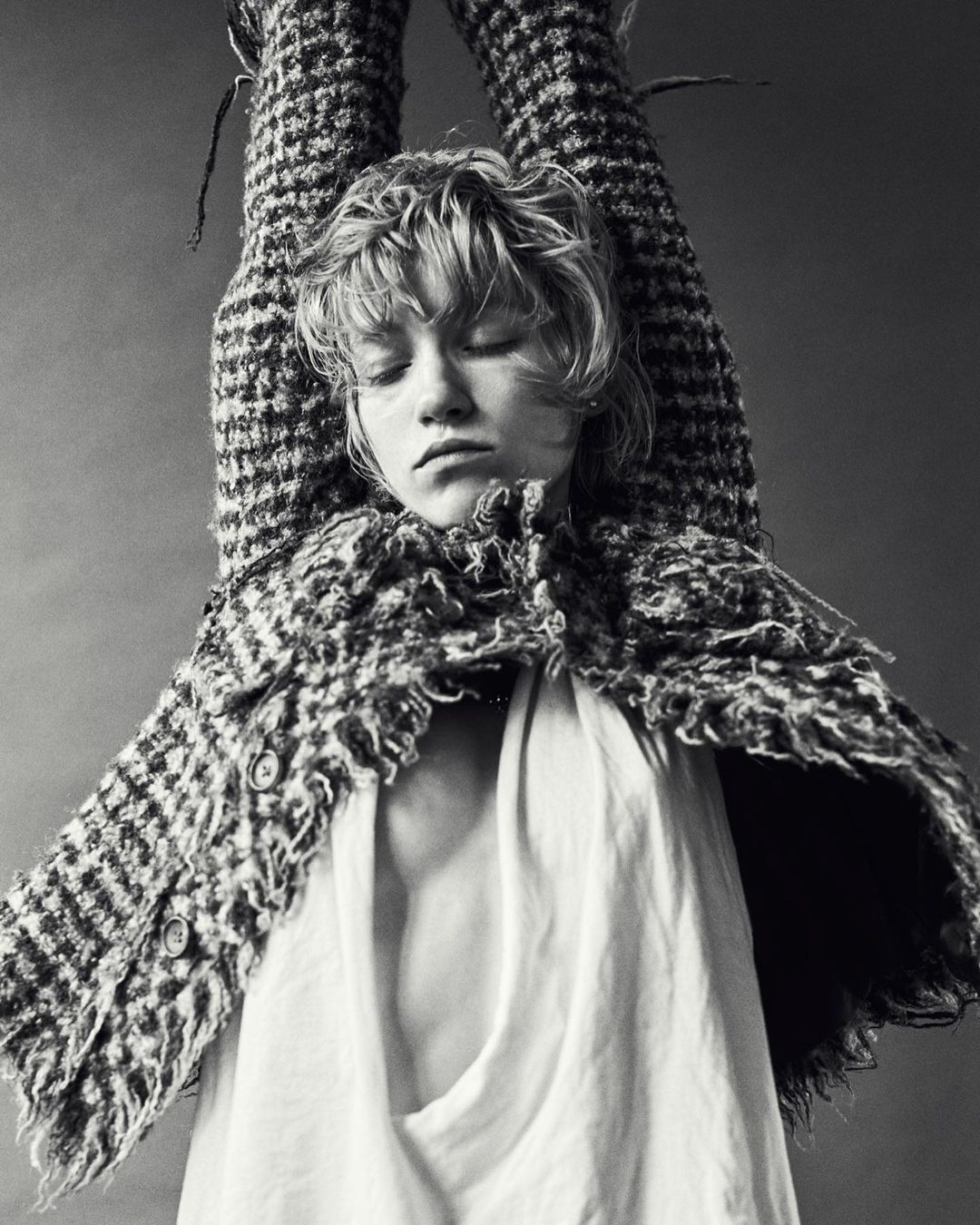 Portrait of a woman with her arms raised, wearing a textured tweed jacket and white top, shot in monochrome by Alessio Albi