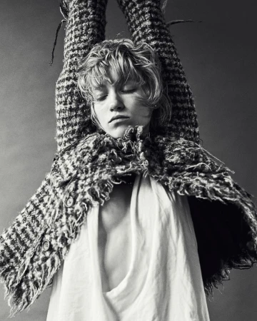 Portrait of a woman with her arms raised, wearing a textured tweed jacket and white top, shot in monochrome by Alessio Albi