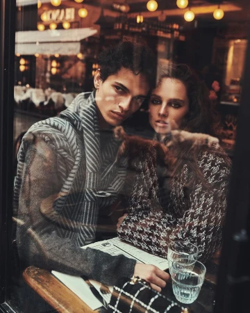 Portrait of an adult male and female couple sitting at a cafe table indoors wearing stylish winter clothing and posing for the camera.