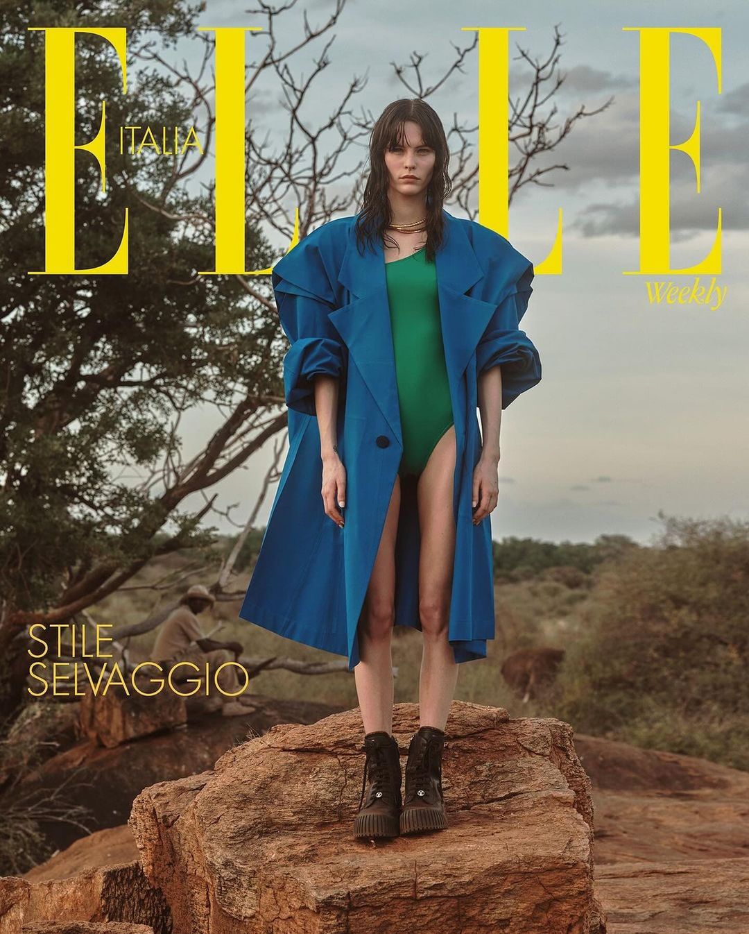 Elle Italia cover features a female model in a teal coat and green bodysuit standing on a rocky surface, with a savanna backdrop.