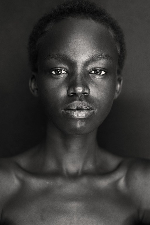 Striking black and white portrait of a young African woman against a dark background, showcasing her natural beauty and elegant features.