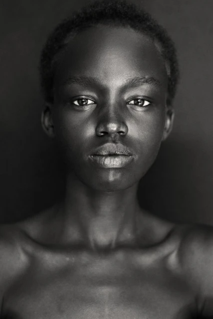 Striking black and white portrait of a young African woman against a dark background, showcasing her natural beauty and elegant features.