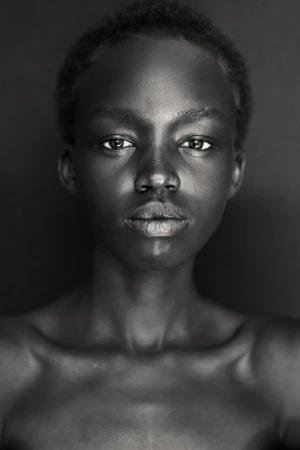 Striking black and white portrait of a young African woman against a dark background, showcasing her natural beauty and elegant features.