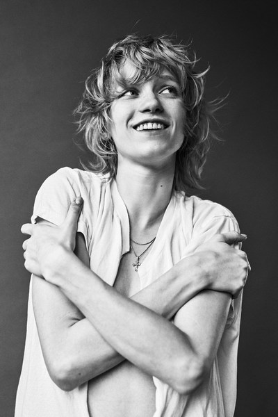 Black and white portrait of a smiling fair-skinned adult female with short wavy blonde hair, arms crossed, wearing a casual top.