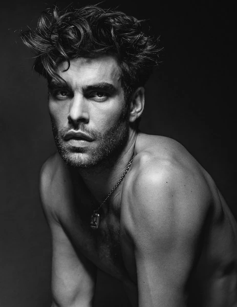 Striking black and white portrait of a handsome, fair-skinned adult male with dark wavy hair, a beard, and a chain necklace.