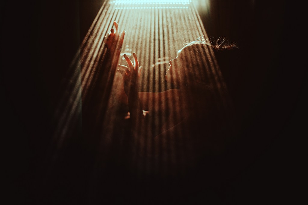 Woman bathed in light, hands raised in a dark setting. Light rays illuminate her silhouette and suggest a sense of mystery and depth.