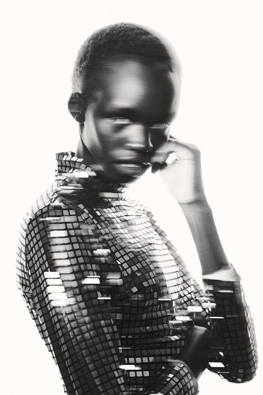 Monochrome portrait of a young woman wearing a square sequined top, with hand near her face, set against a light background.