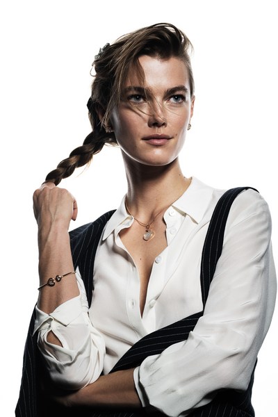 Portrait of a woman with braided hair wearing a white button-down shirt and pinstripe vest in a brightly lit photo studio.
