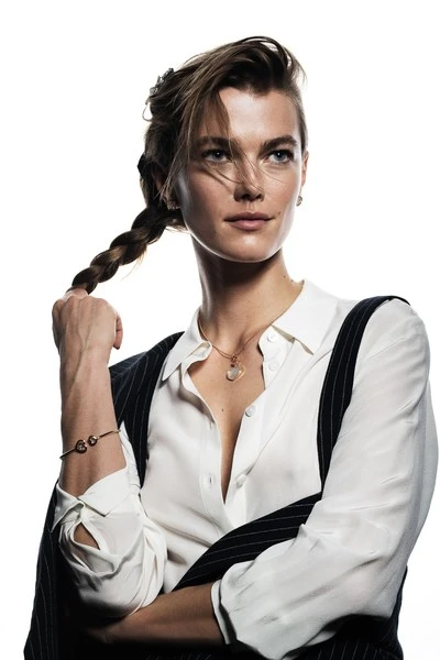 Portrait of a woman with braided hair wearing a white button-down shirt and pinstripe vest in a brightly lit photo studio.