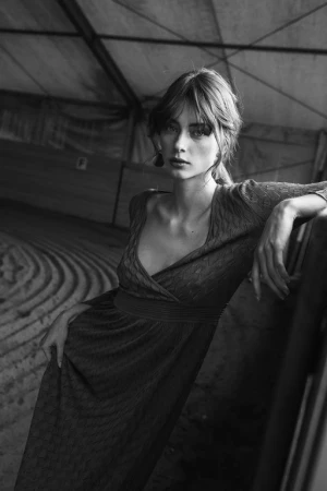 Portrait of a woman wearing a textured long-sleeve dress leaning against a railing in a tent structure by Alessio Albi.