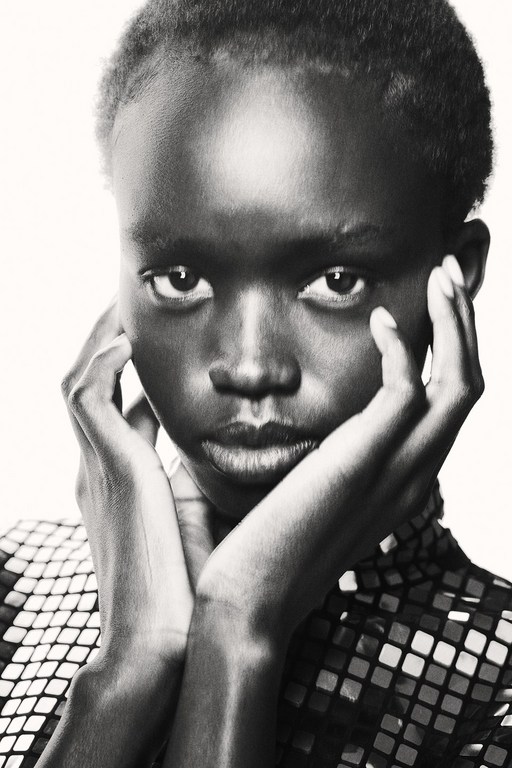 Close-up portrait of a young African-American woman with dark skin, short hair, and a patterned top, posing against a bright background.