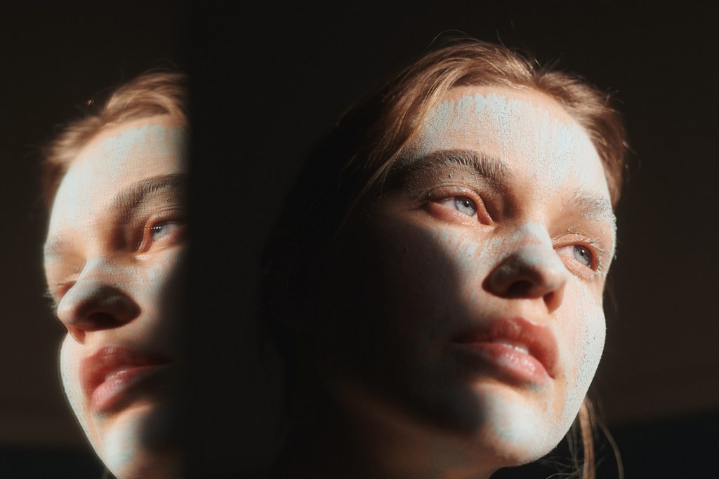 Two adult female faces are illuminated by a bright light, with one face partially obscured by shadow, creating a striking, contrasted portrait.