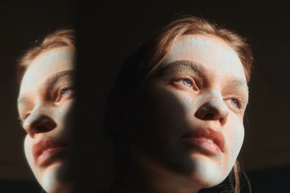 Two adult female faces are illuminated by a bright light, with one face partially obscured by shadow, creating a striking, contrasted portrait.