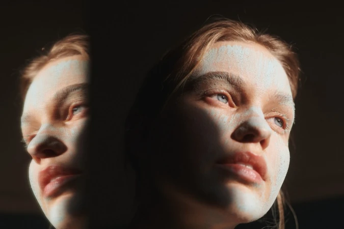 Two adult female faces are illuminated by a bright light, with one face partially obscured by shadow, creating a striking, contrasted portrait.