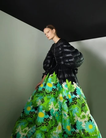 Model wearing a black quilted jacket and vibrant green floral gown against a two-tone wall and black ceiling corner.