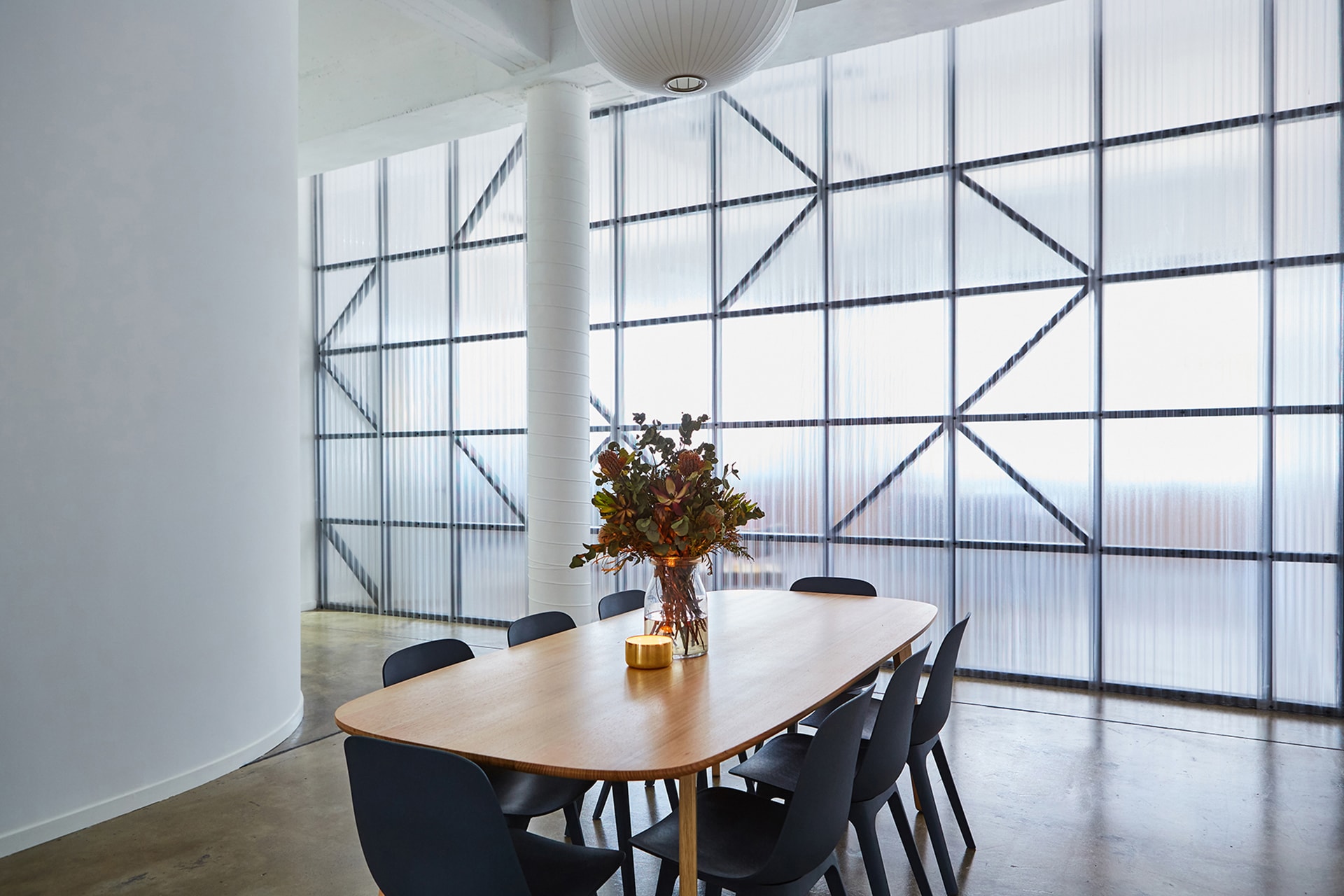 Minimalist interior showcasing a wooden conference table with black chairs, a glass vase centerpiece, and a large window.