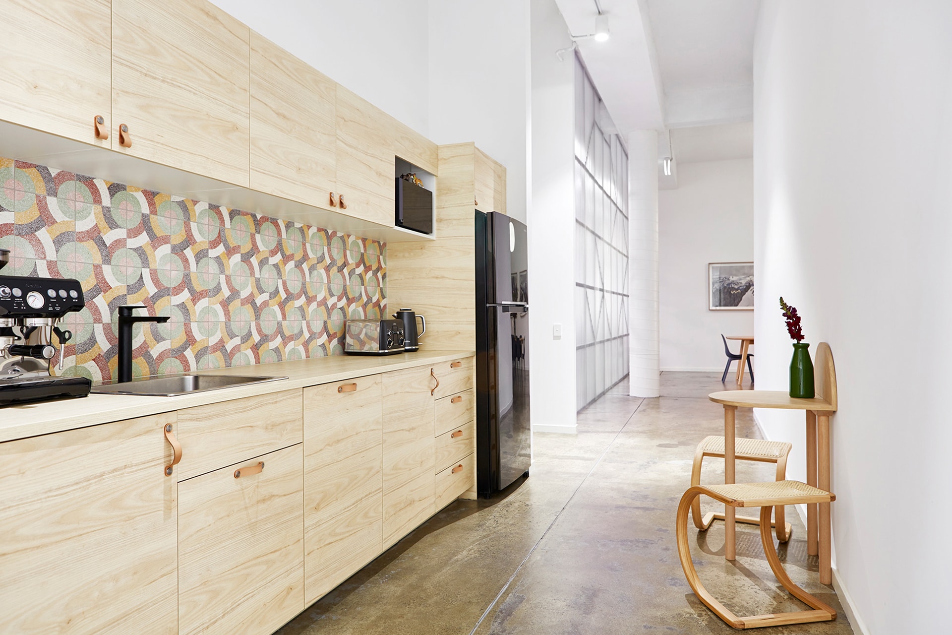 Bright kitchen interior with light wood cabinets, modern appliances, colorful patterned backsplash, and minimalist Scandinavian-style furniture.